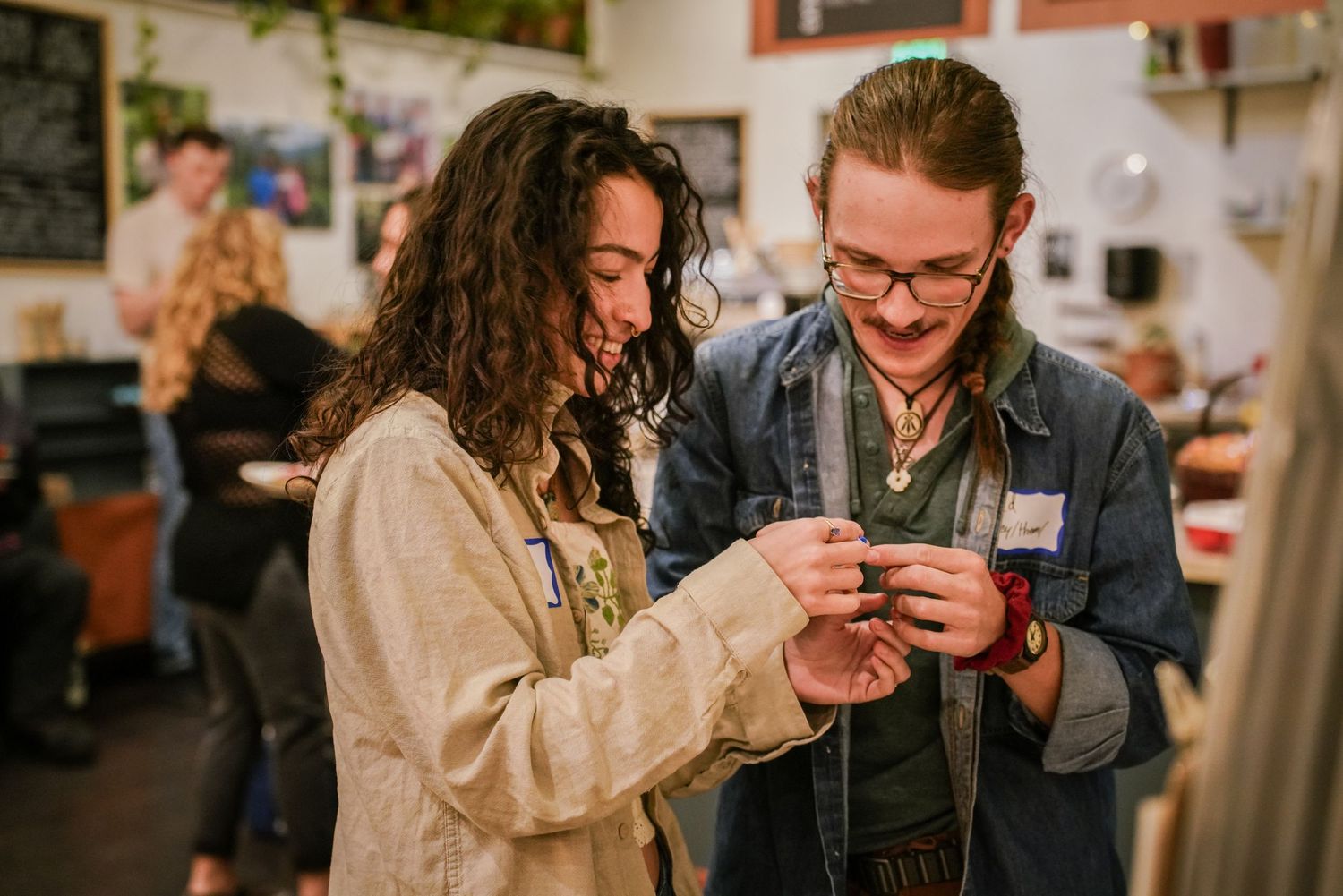 Two young people smile while examining a small object together at a casual indoor social event.