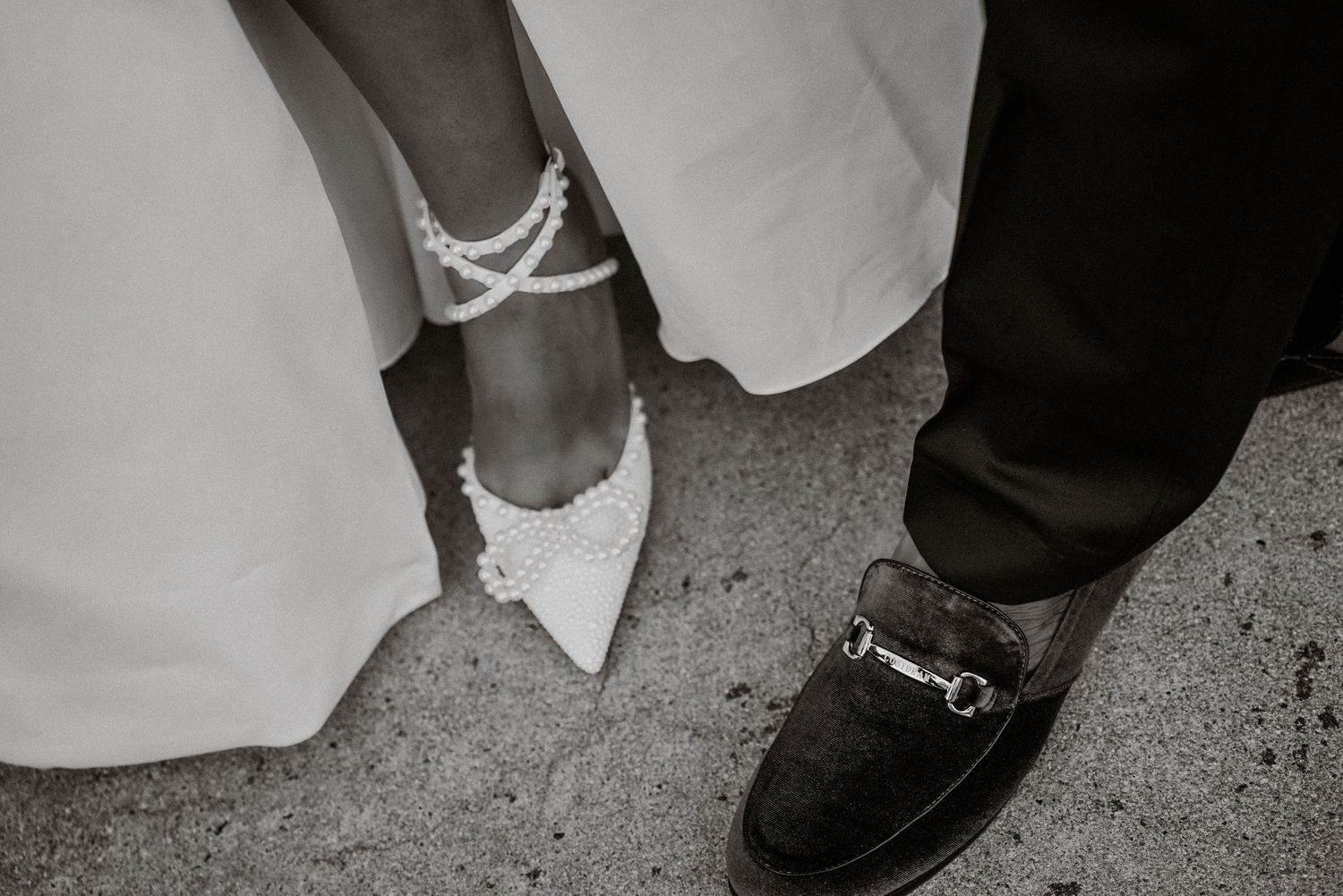 Black and white photo of bride in pearl heels and groom in loafers standing together on their wedding day.