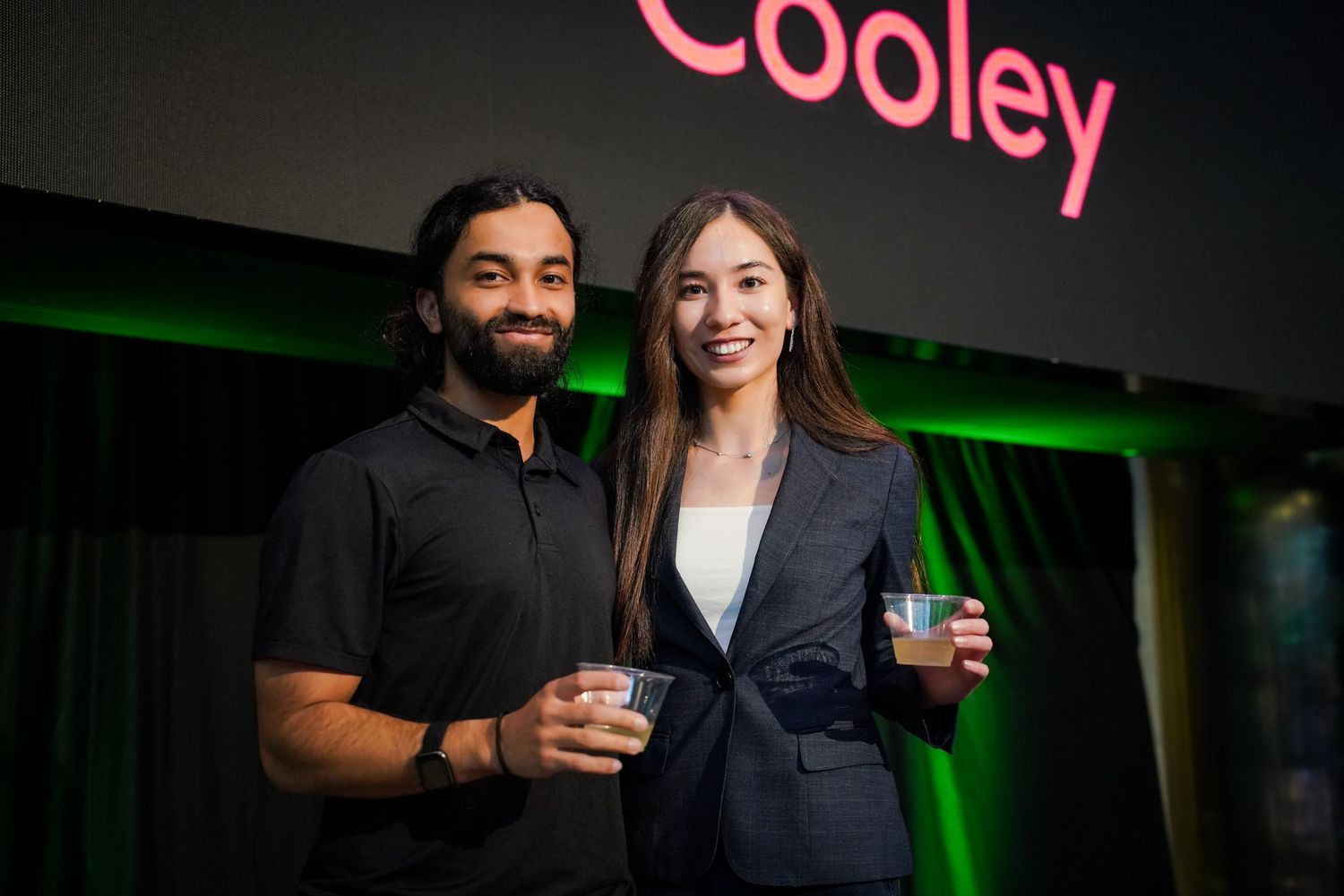 Man and woman smiling together at Cooley corporate networking event with green branded backdrop.