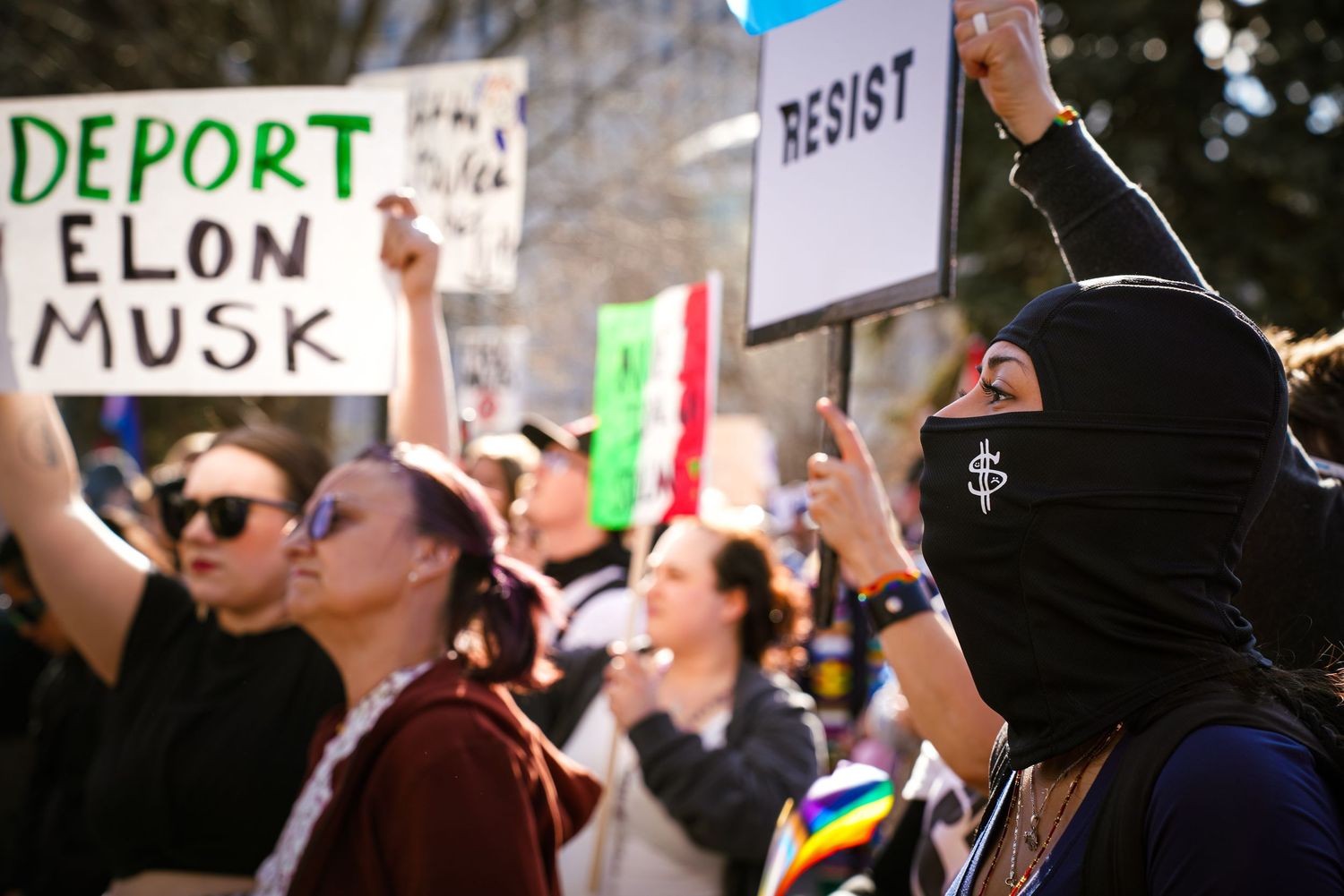 Diverse protesters marching with signs reading Deport Elon Musk and Resist at a political demonstration.