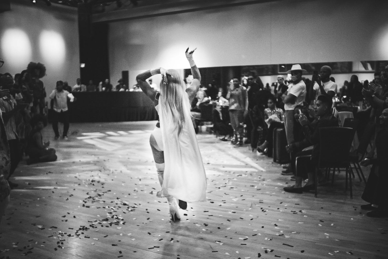 A dancer in white dress performs on a confetti-covered floor at a black and white dance event.