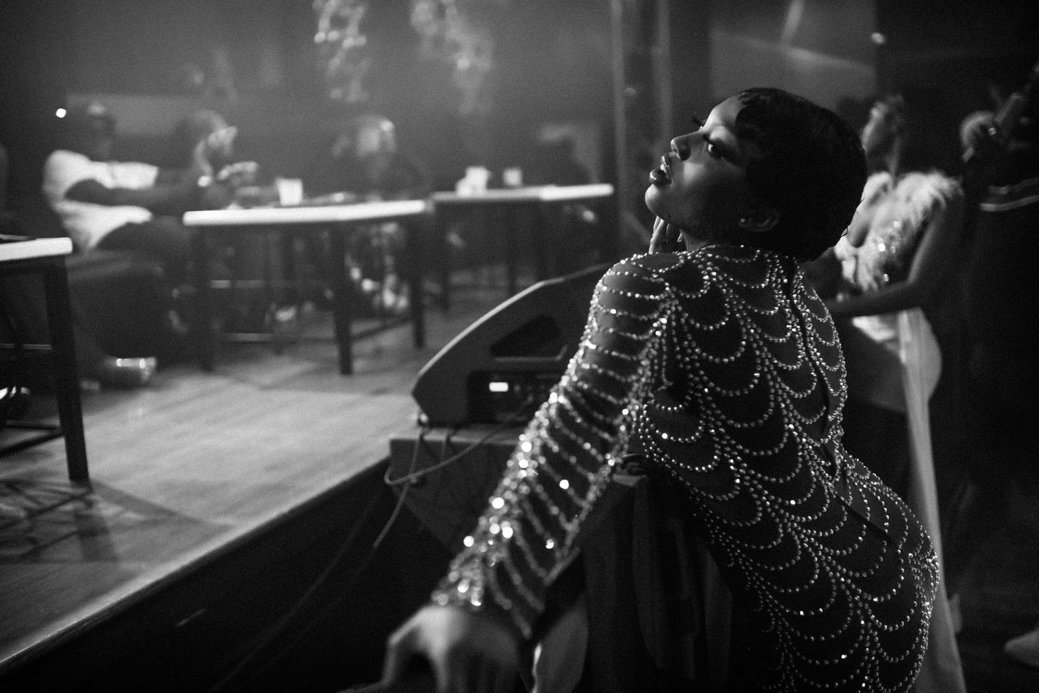Black and white portrait of woman in beaded cape costume reclining elegantly backstage.