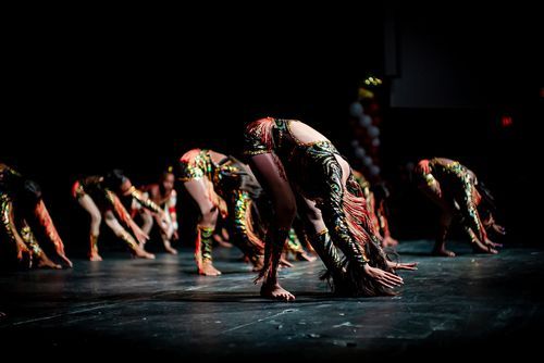 Dancers perform synchronized bowing choreography on a dark stage during a live dance performance.