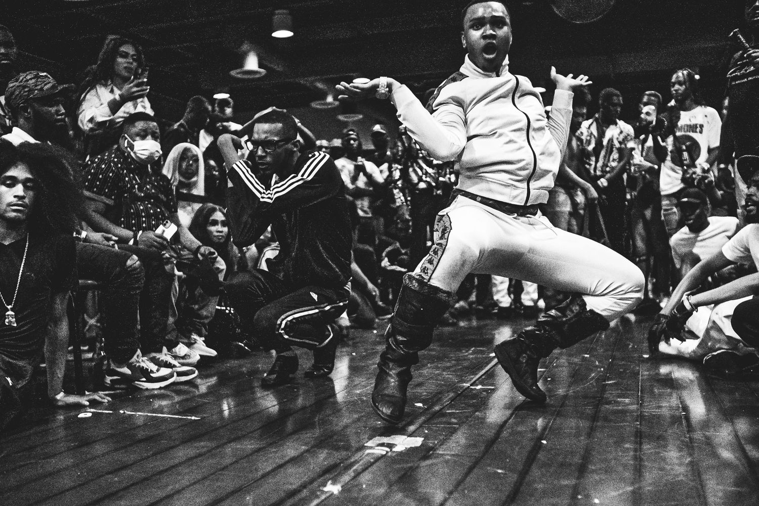 A breakdancer performs an athletic move at a dance battle competition in black and white photo.