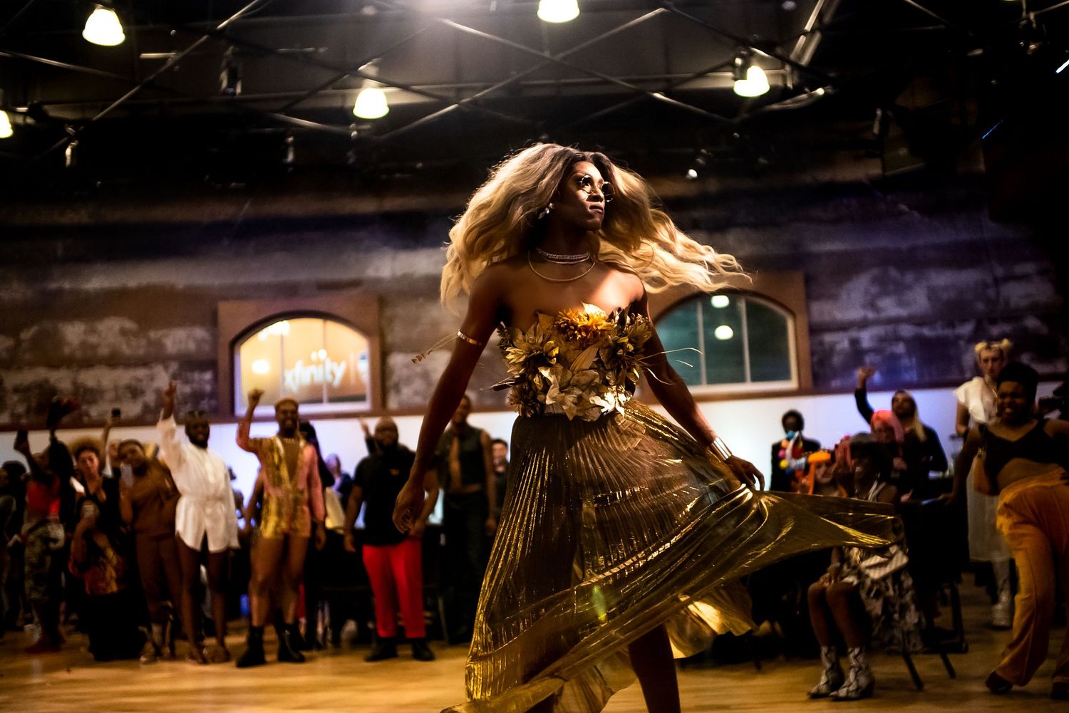 A dancer in a flowing gold dress spins dramatically under stage lights at a performance event.
