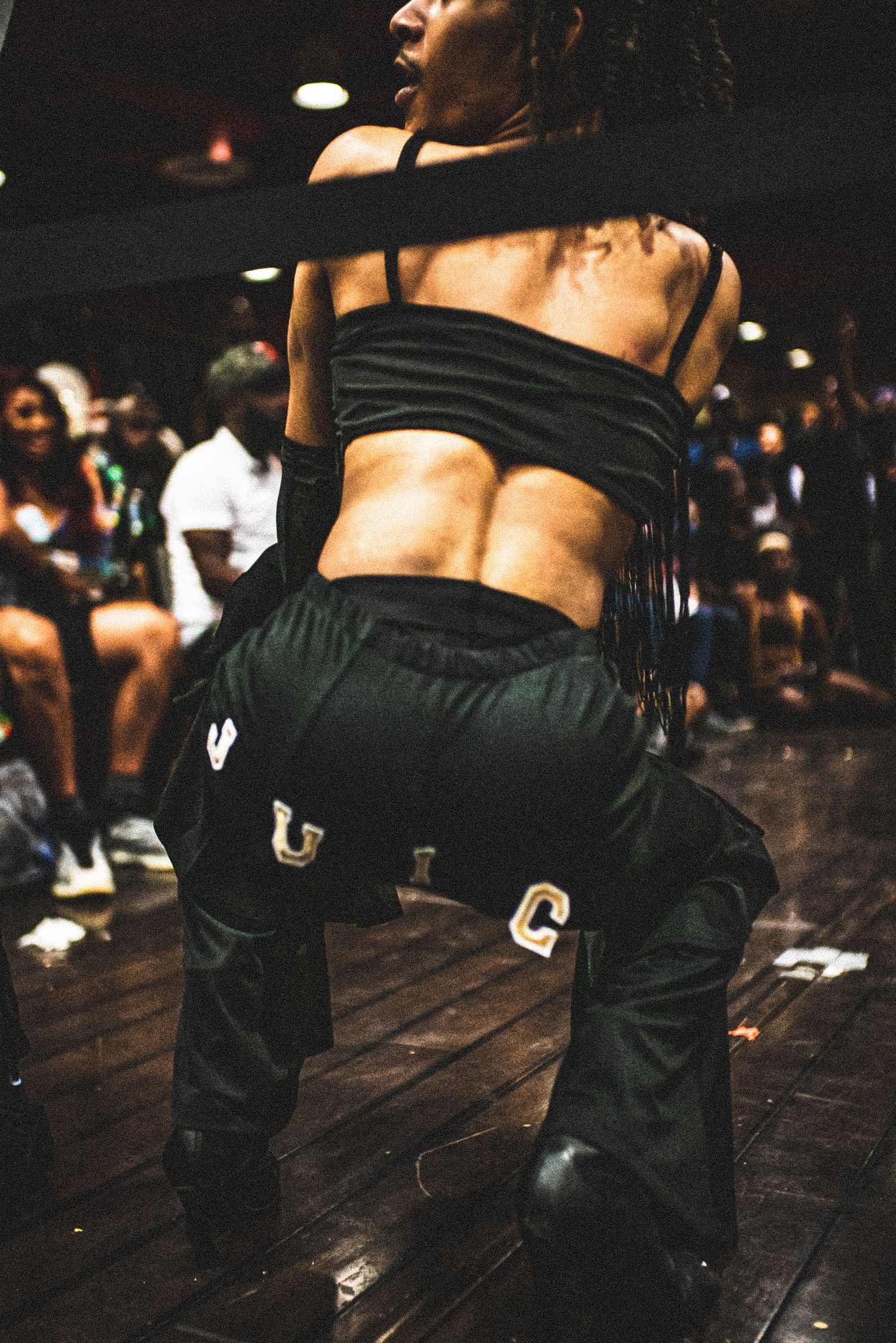A dancer in black crop top and pants performs at an urban dance event on a wooden floor.