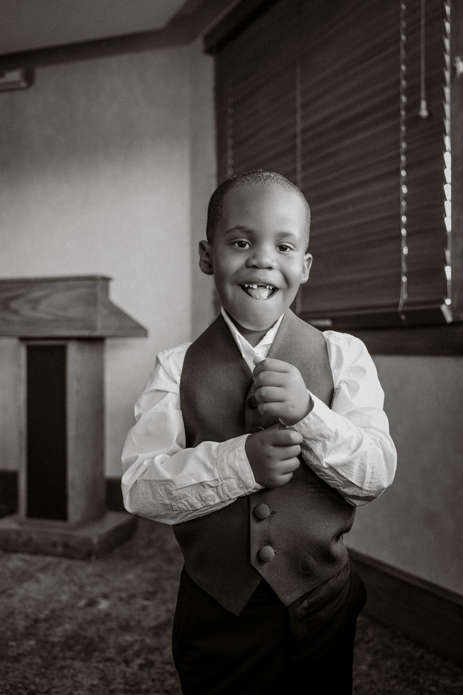 A young boy in a white dress shirt and vest smiles proudly in a black and white portrait photo.
