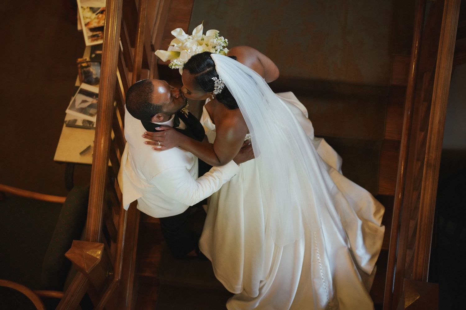 Bride and groom sharing a romantic kiss in a church, captured from above, bride wearing white gown and floral crown.