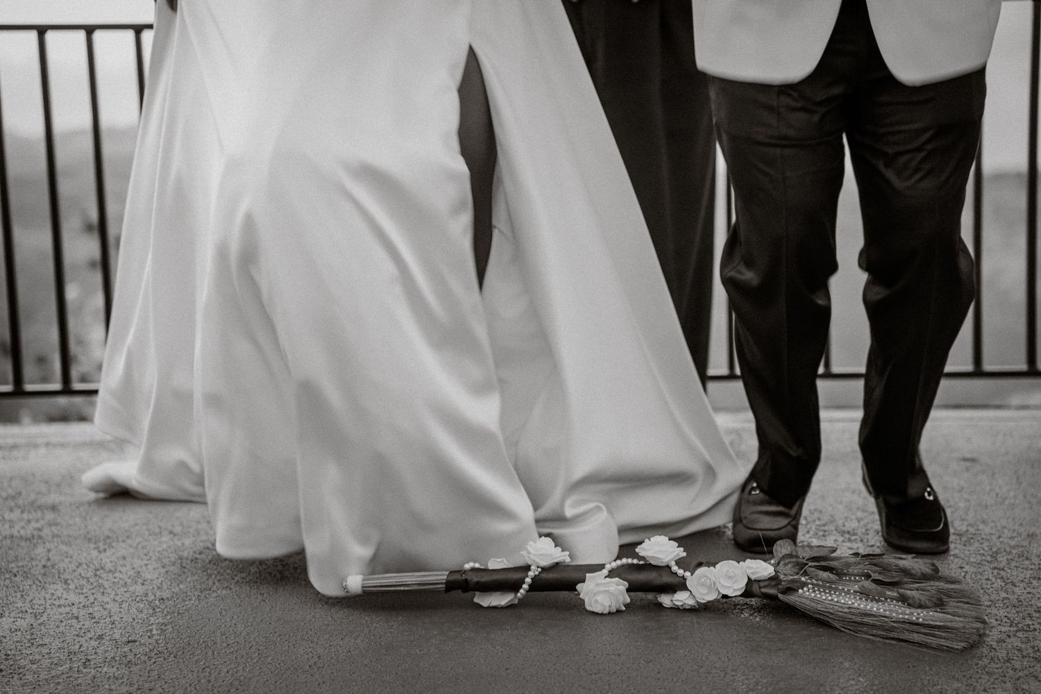 Black and white wedding photo showing bride in white gown and groom in dark suit standing together with floral details on ground.