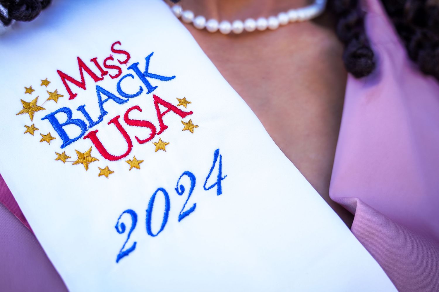 Miss Black USA 2024 embroidered white sash with gold stars worn by a pageant contestant.