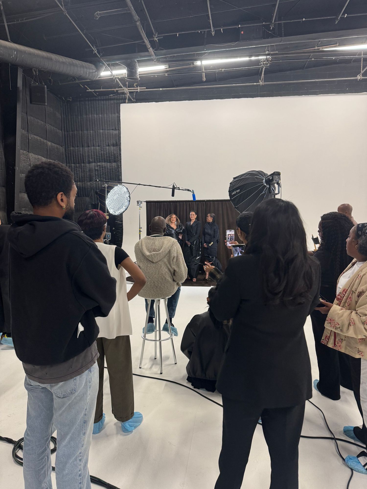 Film crew and students gathered around a subject during a professional photo shoot in a white studio.