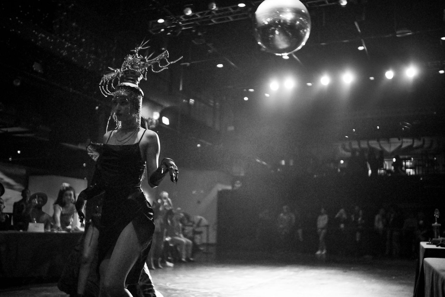 Black and white photo of performer on stage under disco ball at nightclub event.