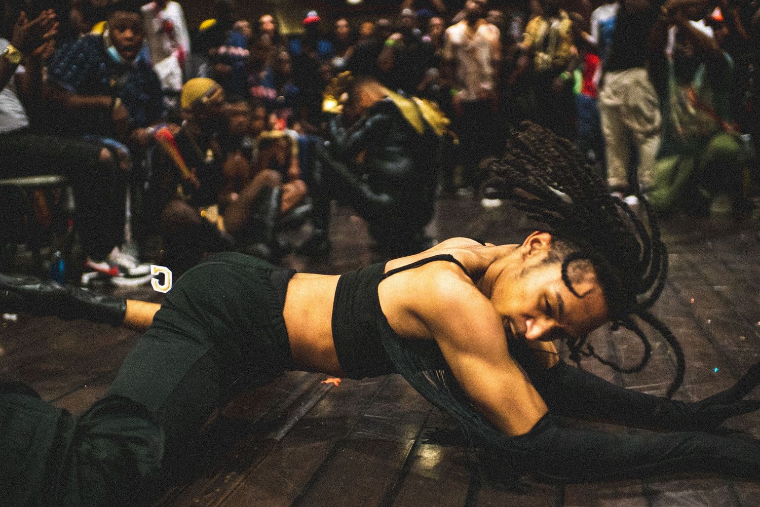 Dancer with dreadlocks performing a dramatic floor pose at a live cultural event.