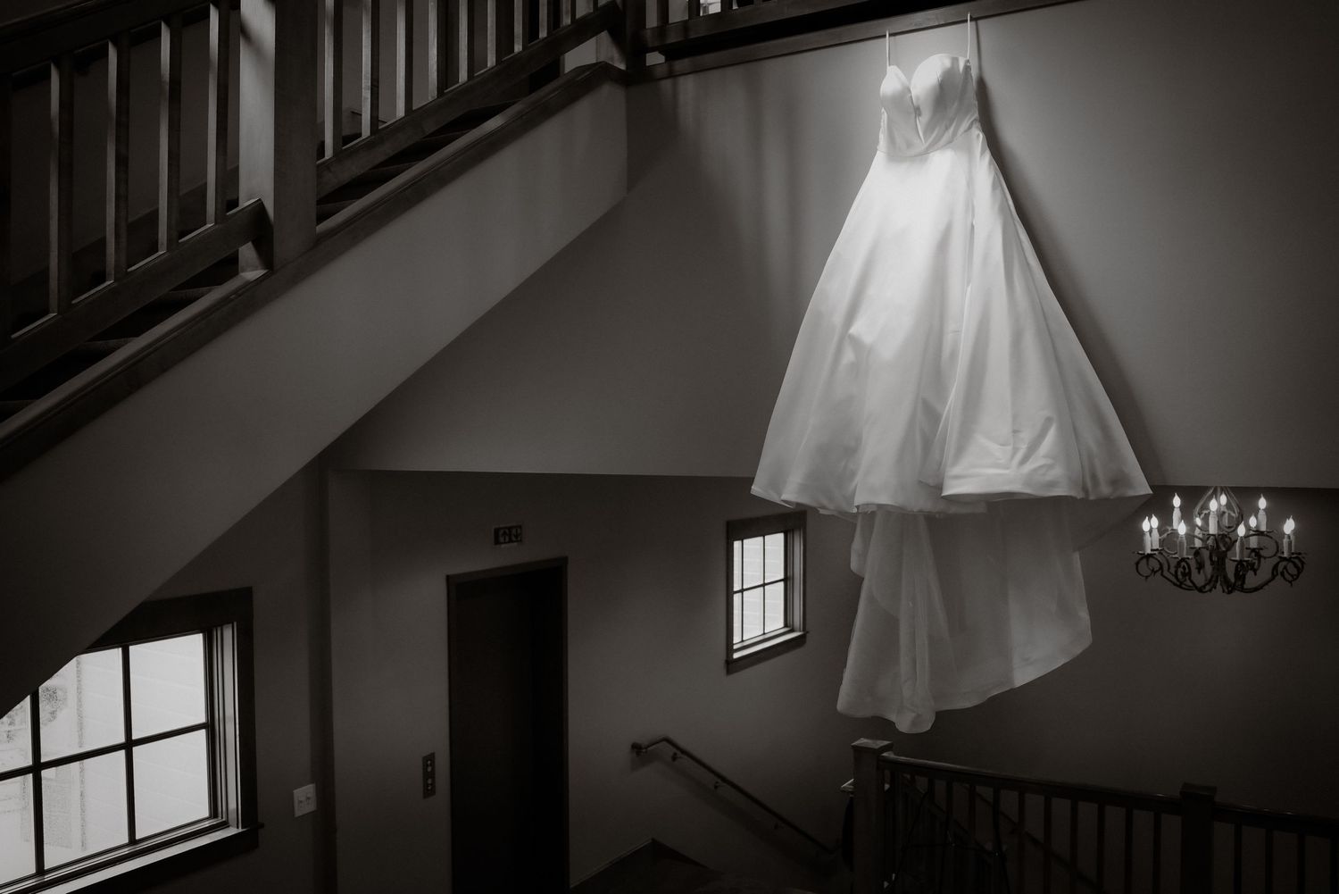 White wedding dress hanging from staircase banister in elegant black and white photography.