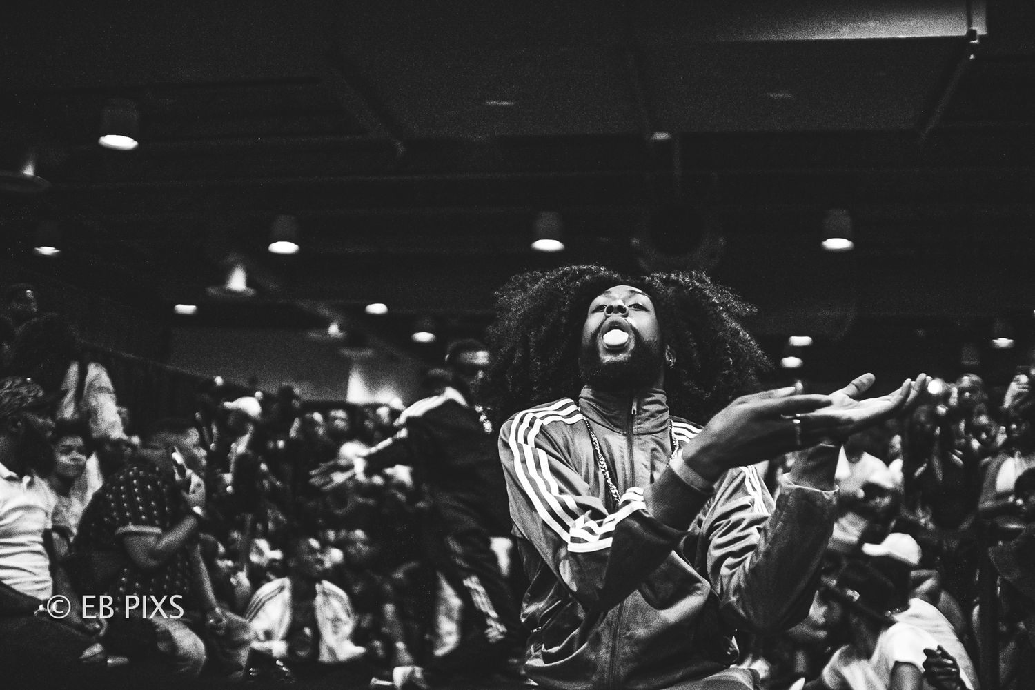Black and white photo of a woman with natural hair singing passionately at a crowded indoor event.