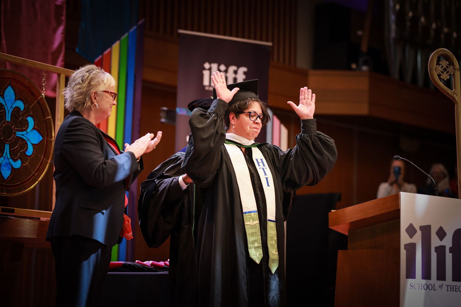 Graduate raises hands in celebration on stage at ILIFF School of Theology commencement ceremony.