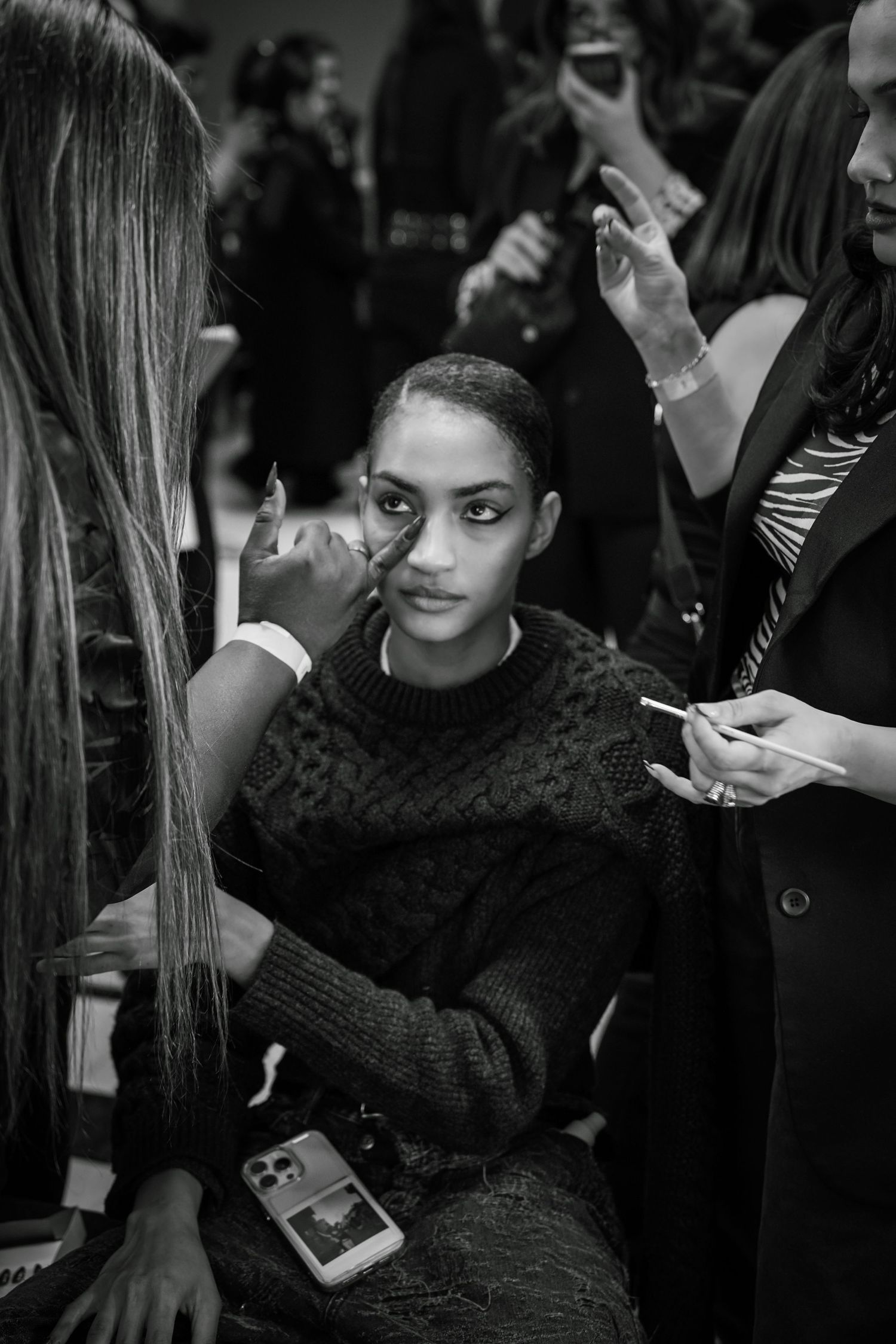 Black and white photo of a model getting makeup applied backstage at a fashion show.