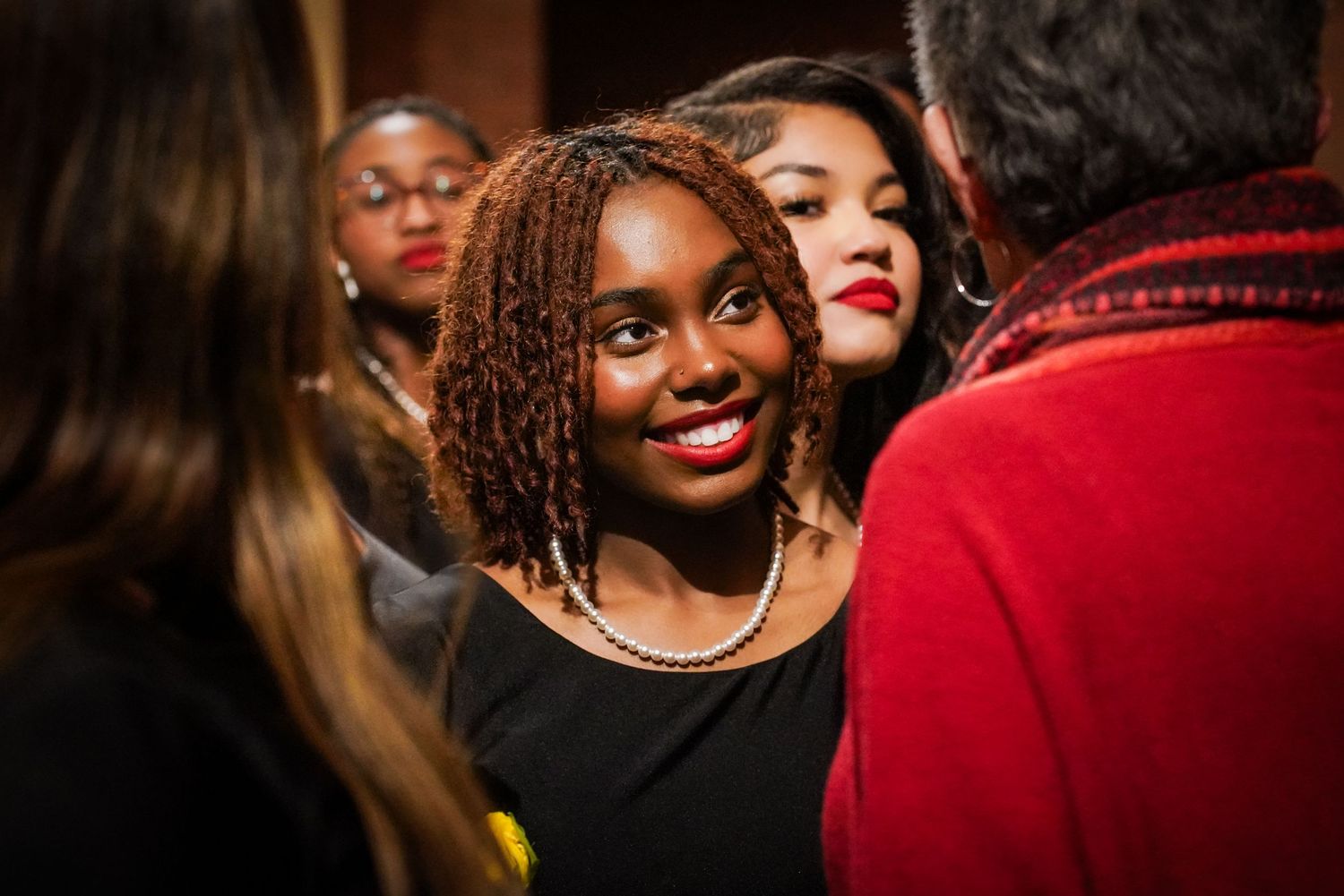 Smiling young Black woman in black dress surrounded by people at a formal church gathering event.