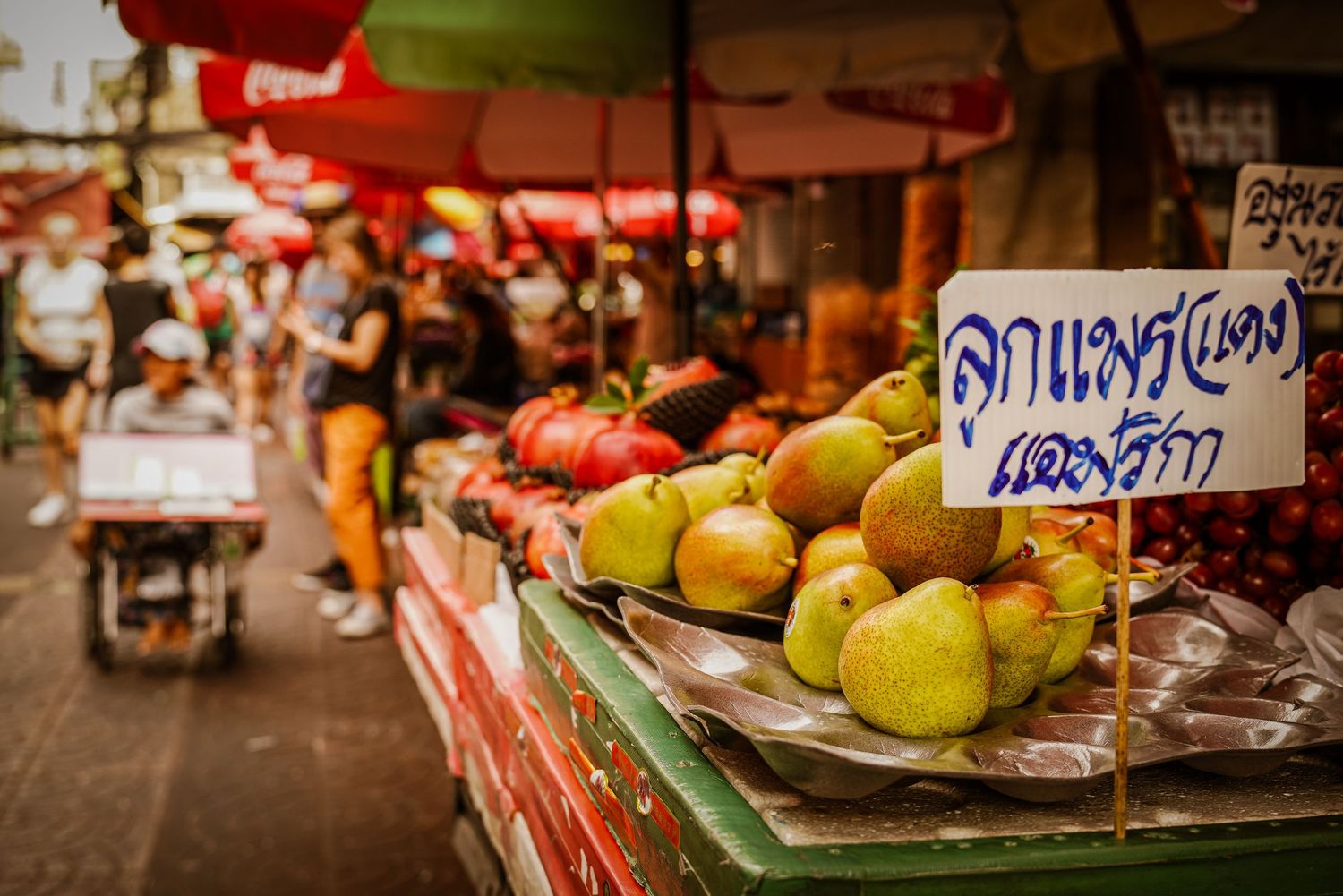 Fresh pears displayed on a vibrant red market stall with Thai language signage.
