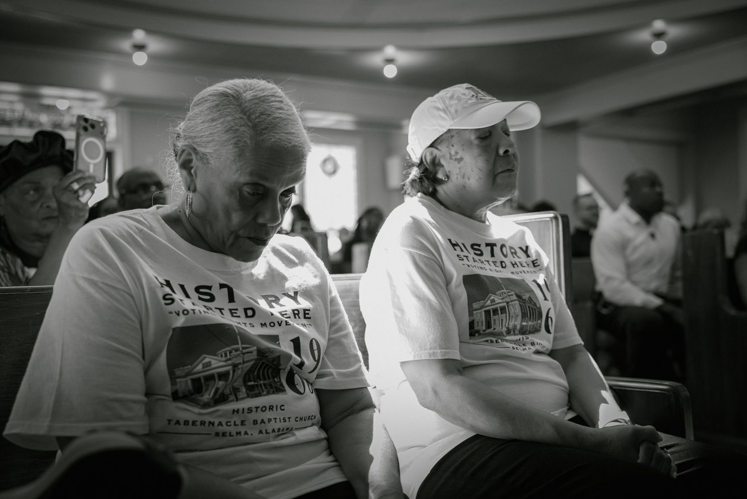 Two elderly people wearing matching event t-shirts sit together in black and white photo.