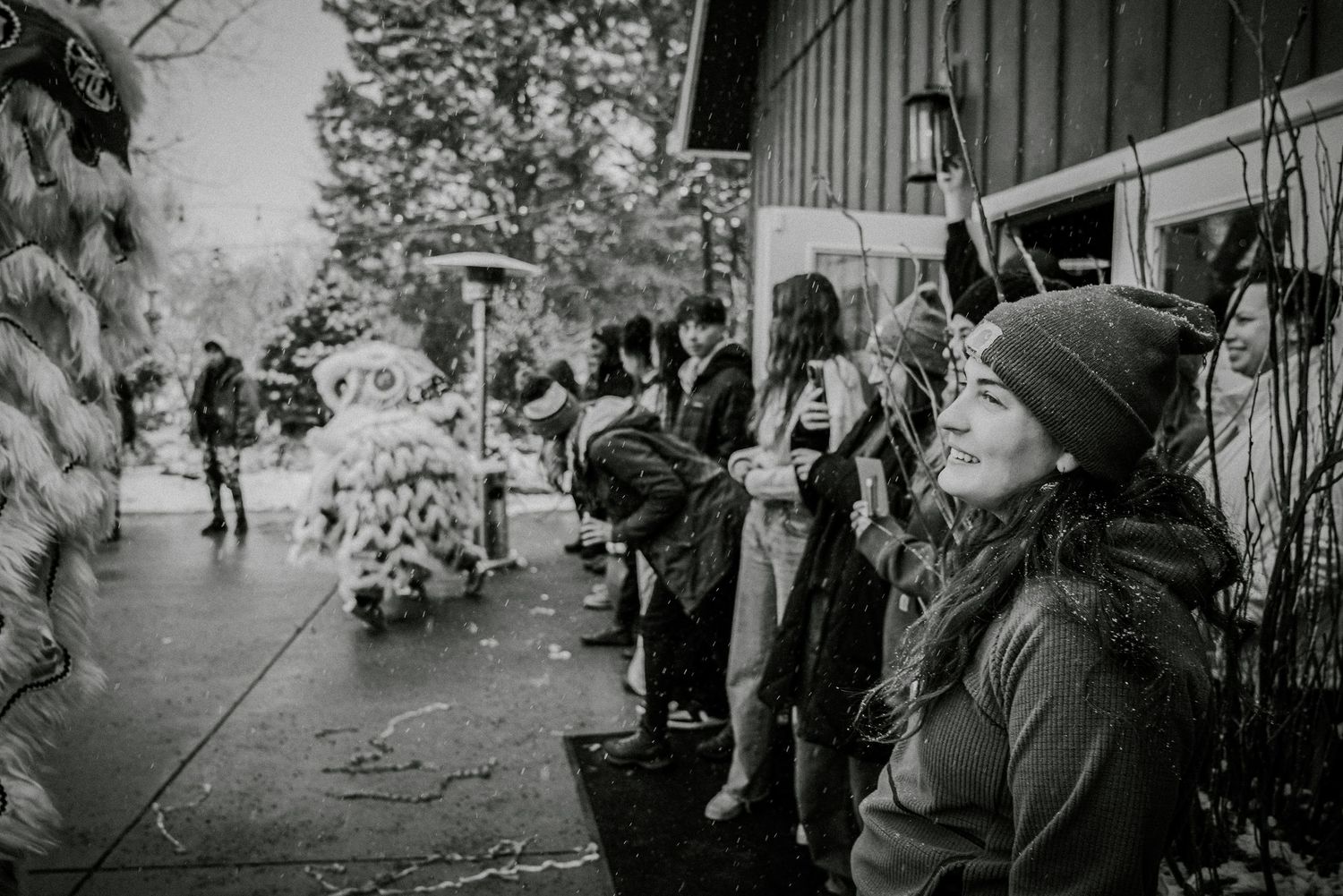 Black and white photo of smiling crowd watching a traditional lion dance performance outdoors at a cultural celebration.