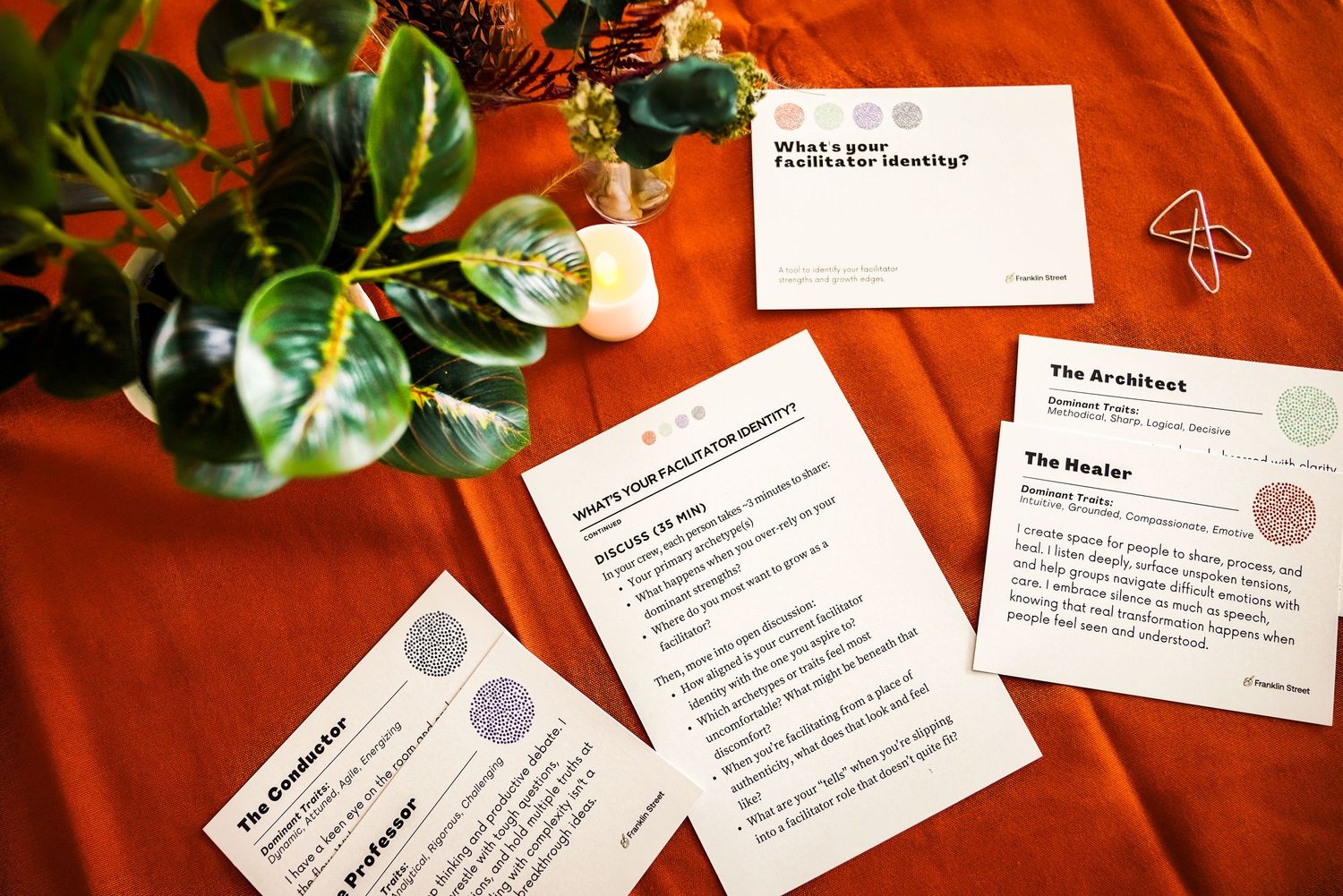 Facilitator identity cards spread on a red table with a plant, featuring roles like The Arabist and The Healer.
