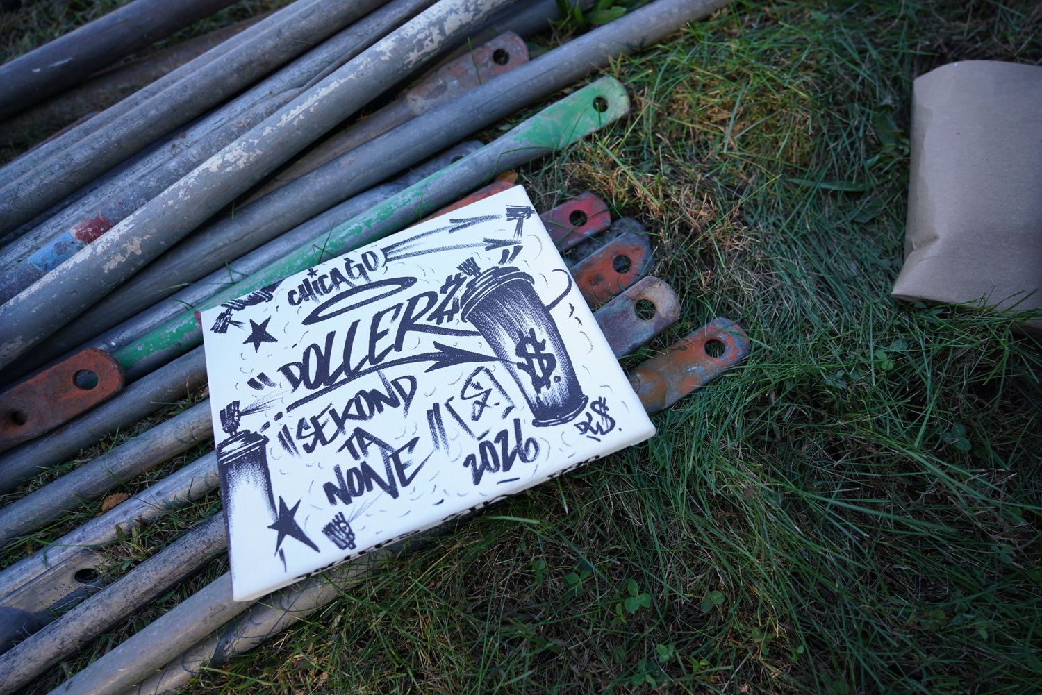 Hand-lettered Chicago Roller Derby sign on white board lying in grass beside stacked metal scaffolding poles and rusty clamps.