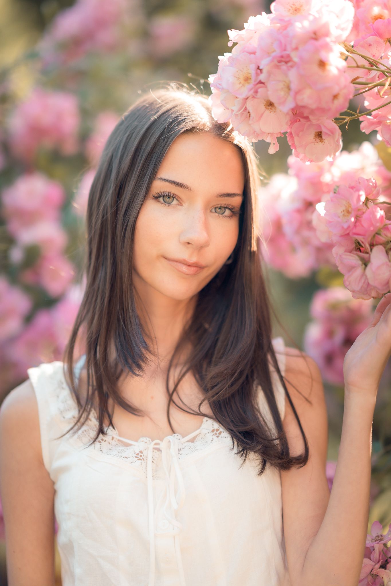 Beautiful young brunette woman standing near pink cherry blossom flowers in soft natural sunlight.