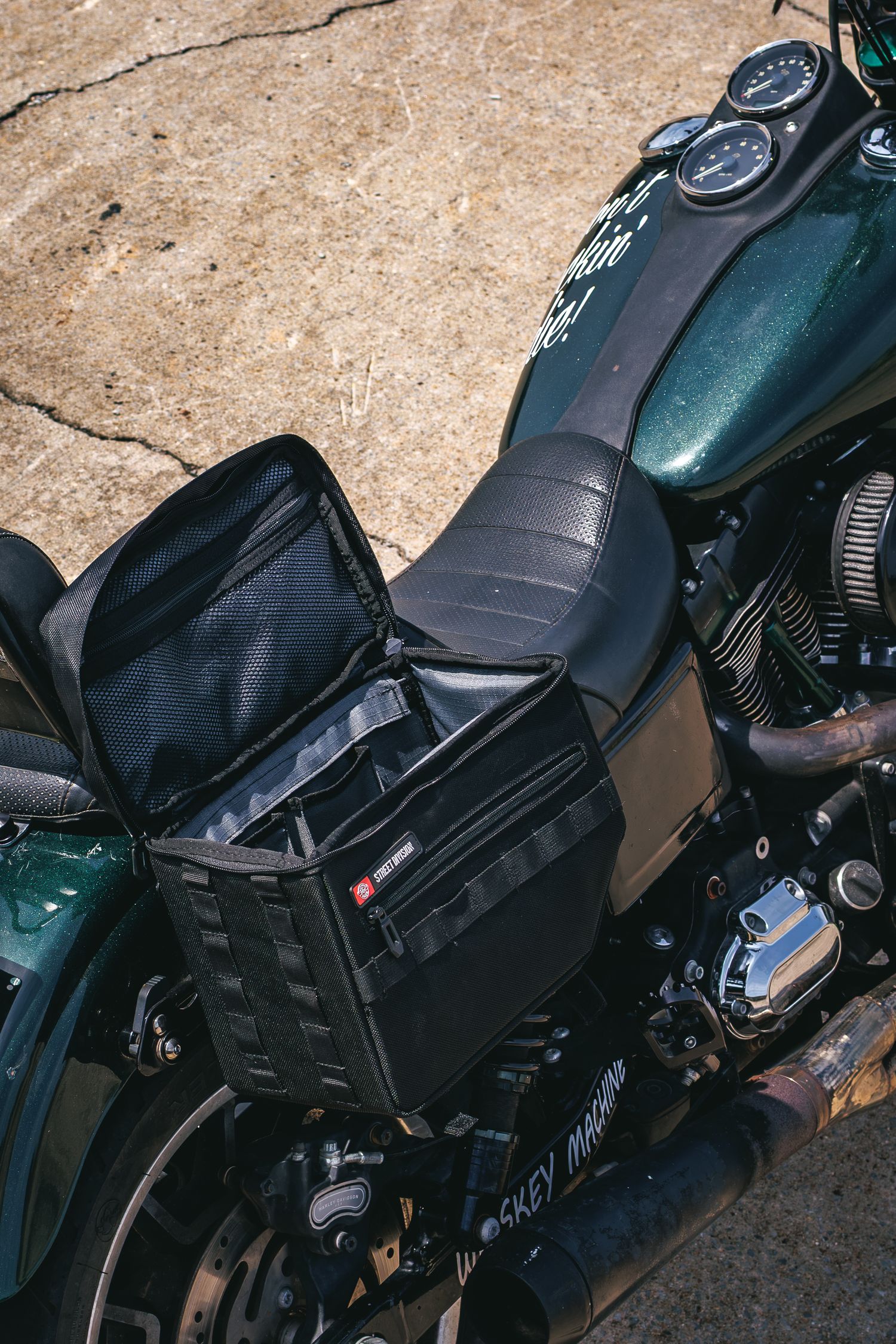A black saddlebag sits open on a green Harley-Davidson motorcycle parked on a concrete surface.