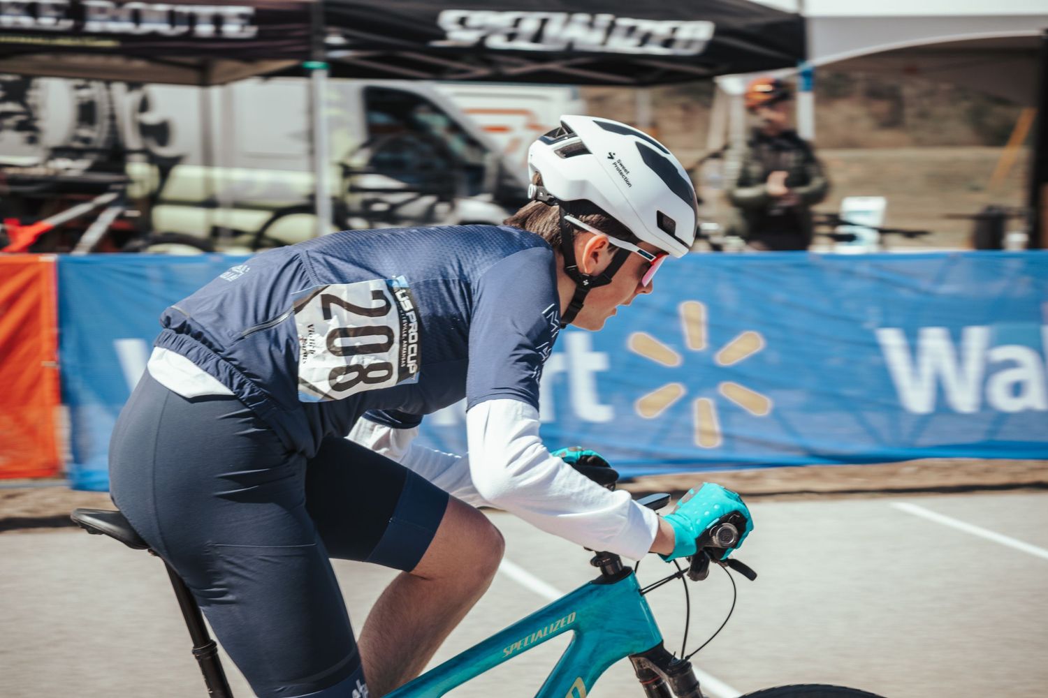 Female cyclist wearing number 208 competing in a road cycling race near a Walmart-sponsored event.