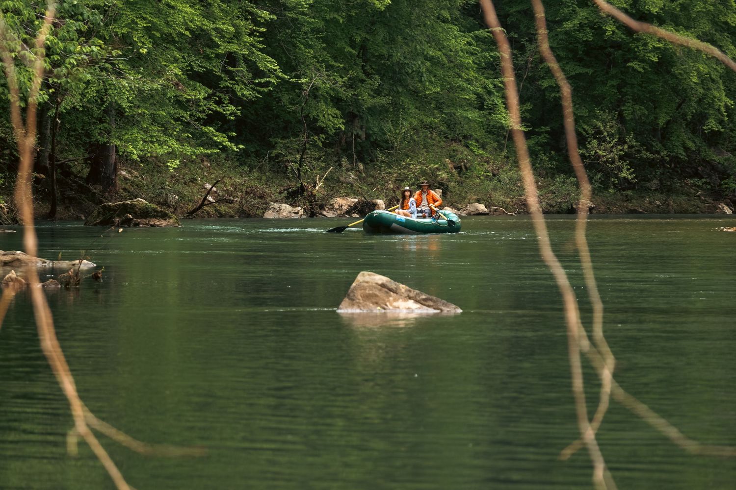 People rafting on a calm green river surrounded by lush forest trees.