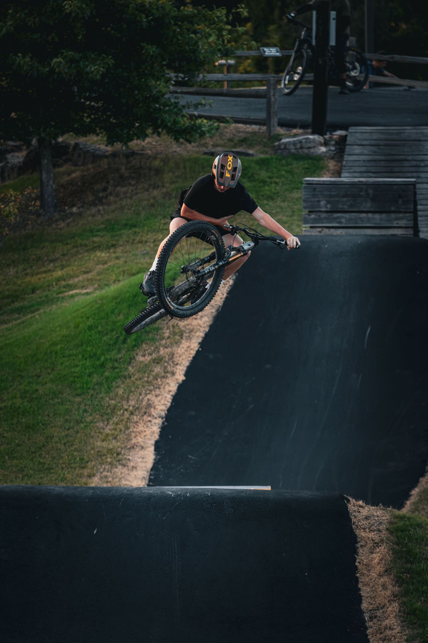BMX rider performing a trick on a pump track at an outdoor bike park.