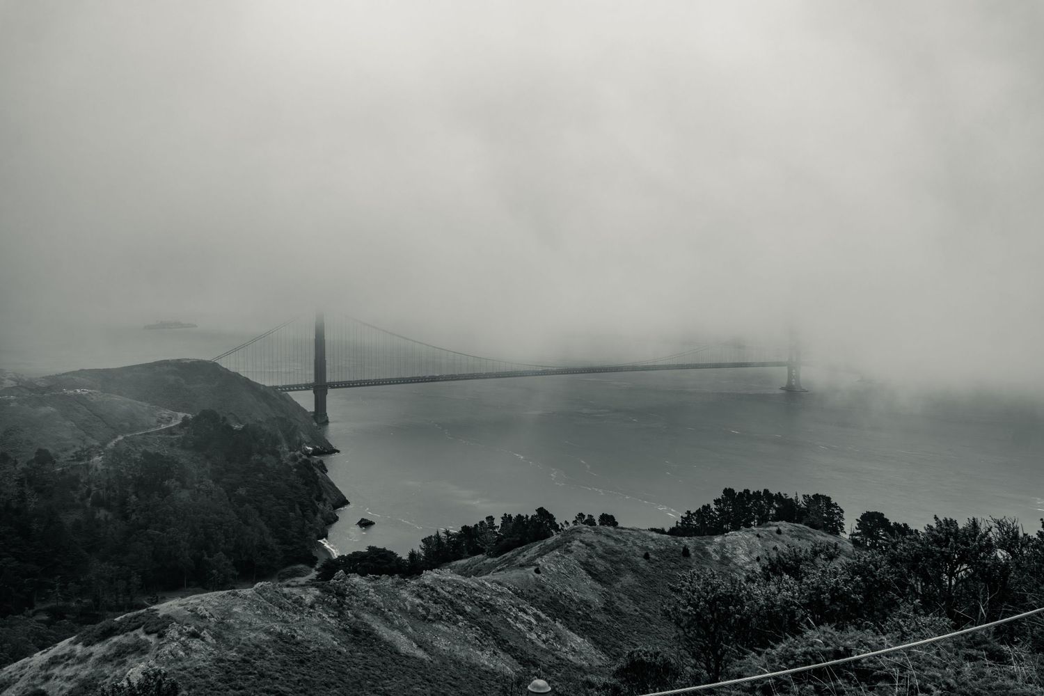 Golden Gate Bridge shrouded in dense fog over San Francisco Bay in moody black and white photography.