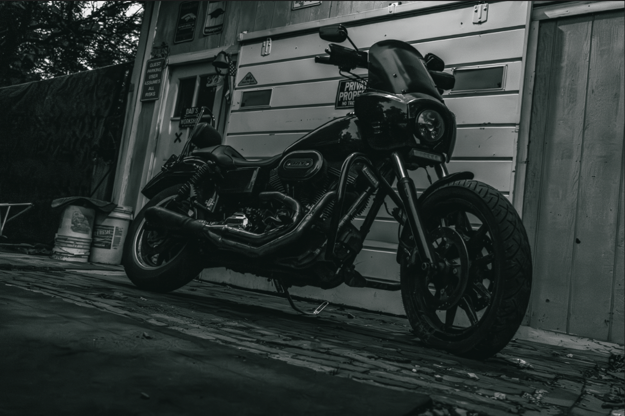 Black and white photo of a custom bobber motorcycle parked outside a building on a wet street.