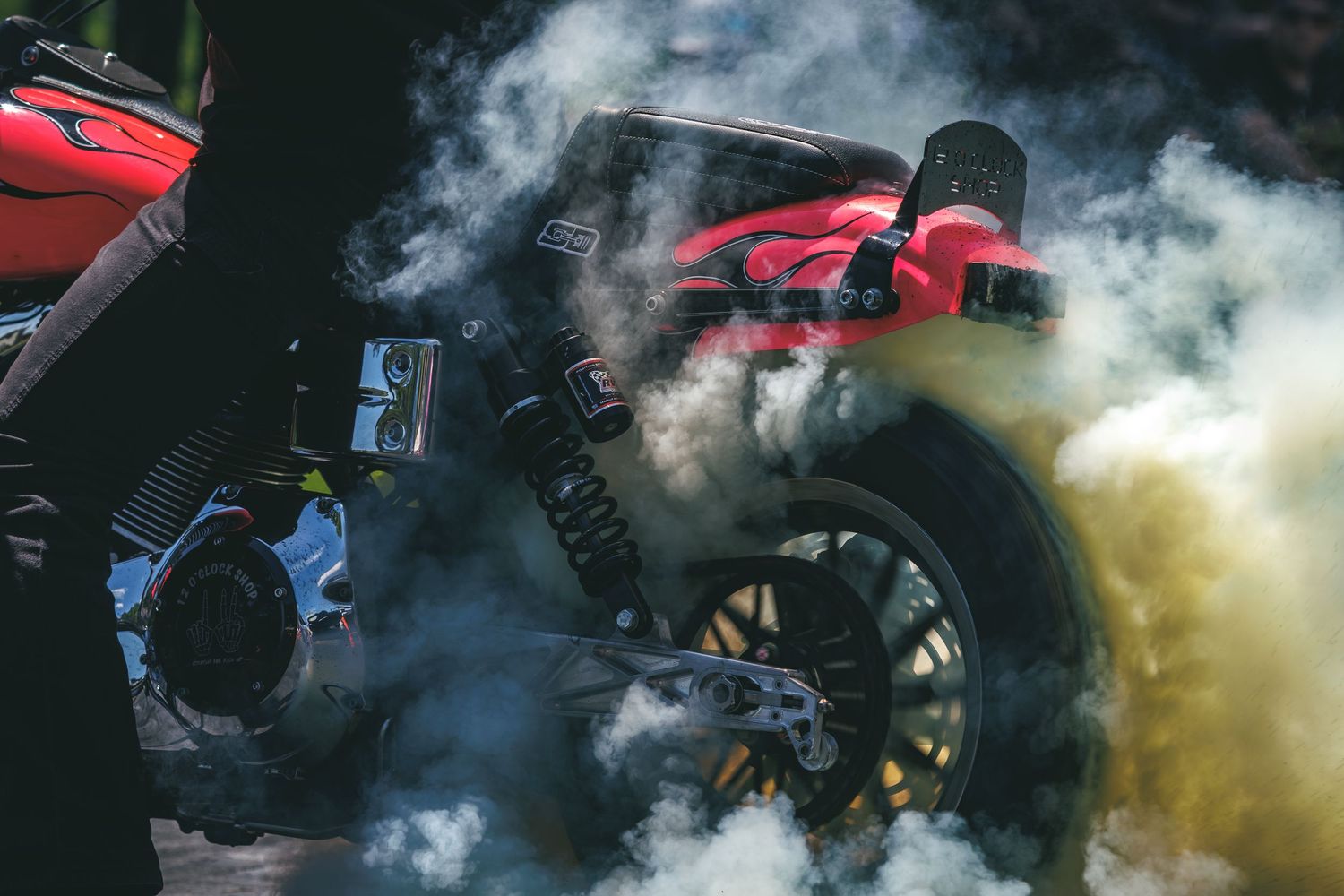 Red motorcycle performing a burnout surrounded by thick white smoke outdoors.