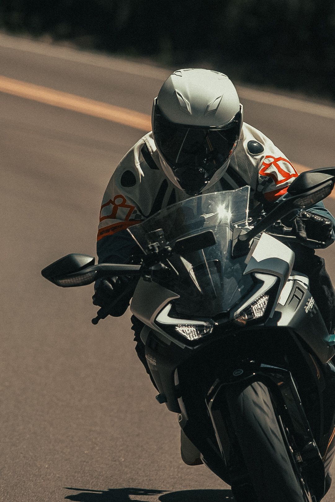 A motorcycle rider in a white helmet leans forward on a sport bike while riding on an open road.