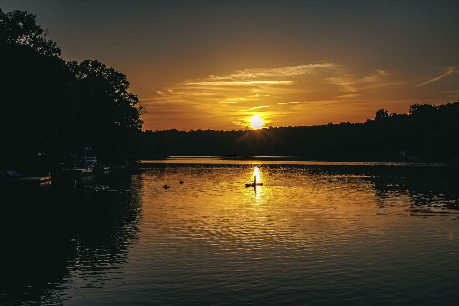 Golden sunset reflecting on a tranquil lake with a silhouetted paddleboarder in the distance.