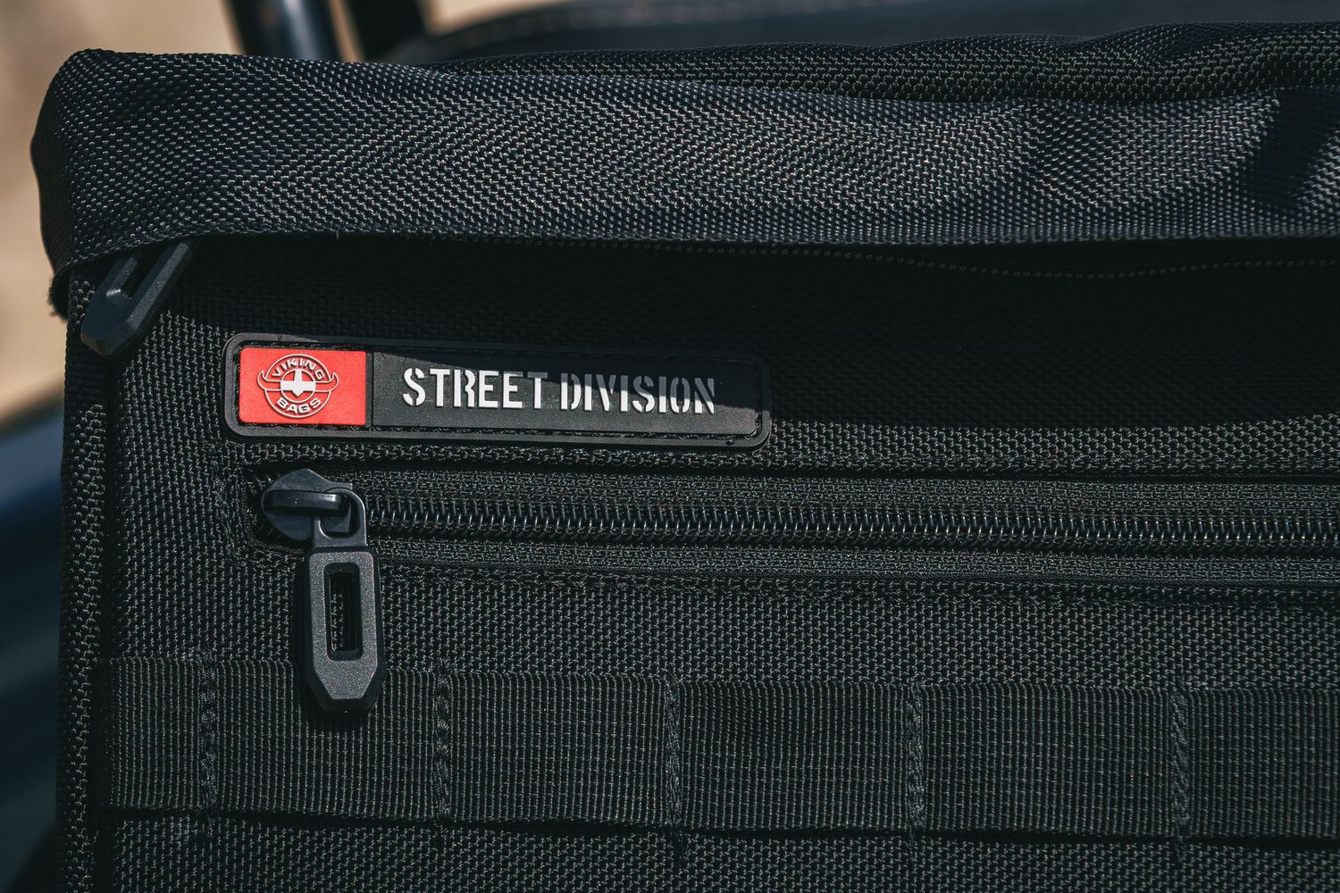 Close-up of a black tactical bag featuring a Street Division branded zipper pull and Swiss flag patch.