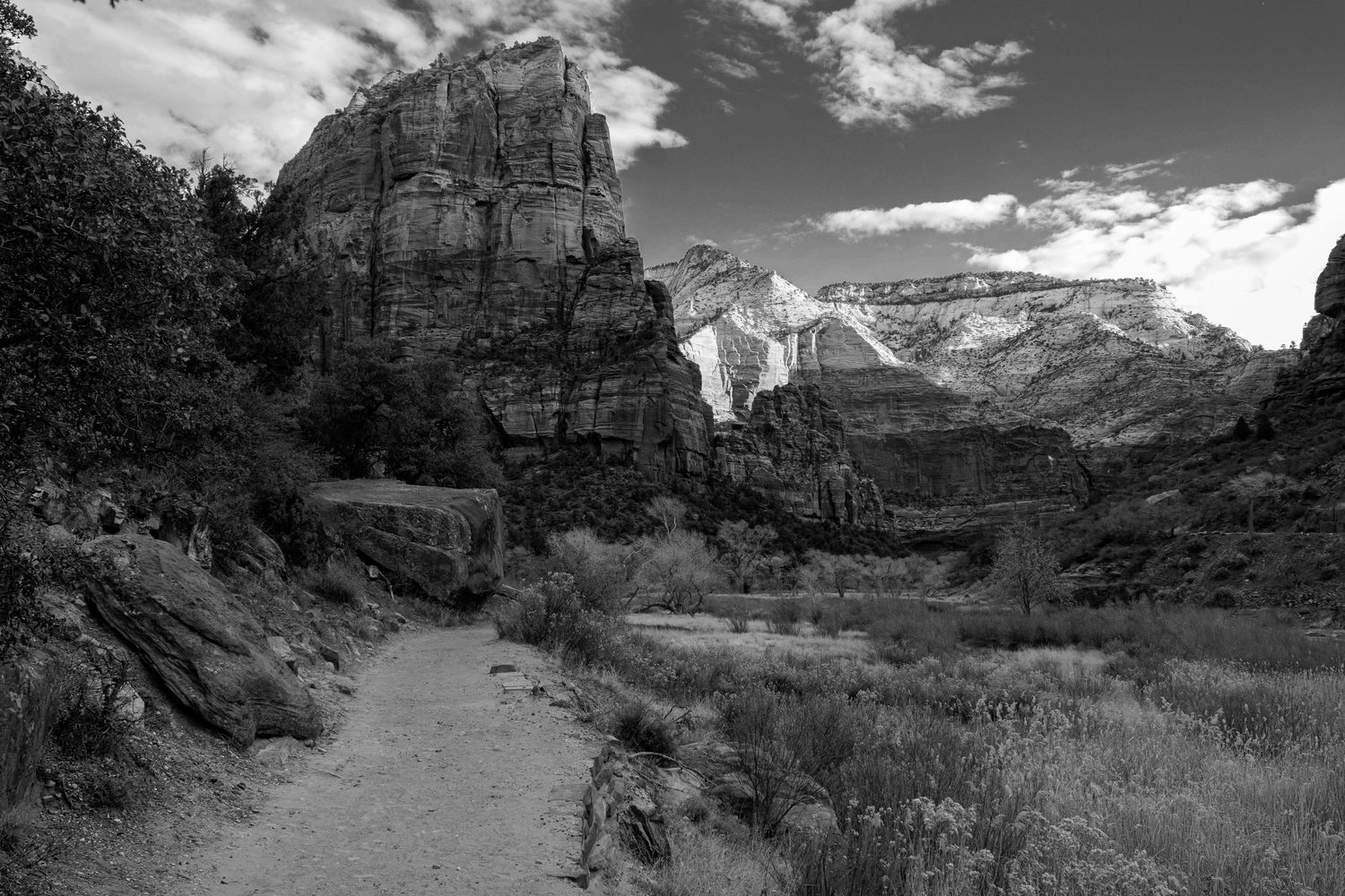 Black and white trail path through Zion National Park with towering sandstone cliffs and cloudy sky.