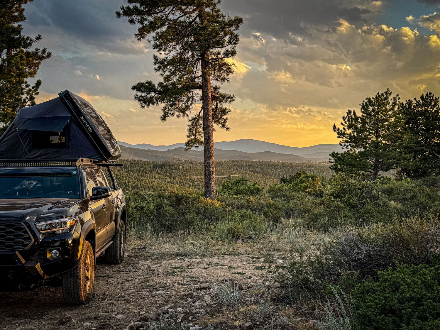 Truck with rooftop tent camping at sunset in a scenic mountain landscape.