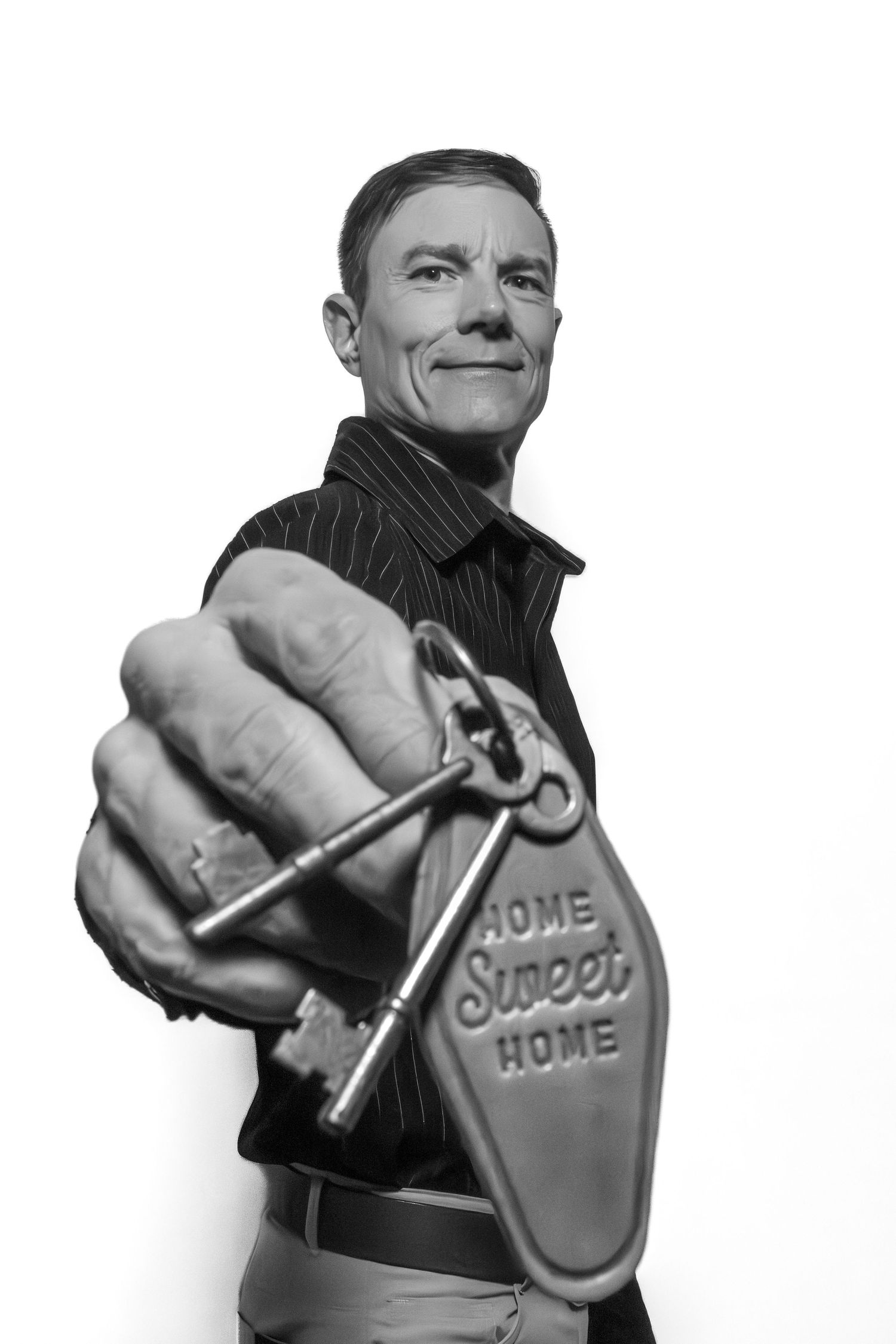 Man in black shirt holding out vintage keys with Home Sweet Home keychain, black and white photo.