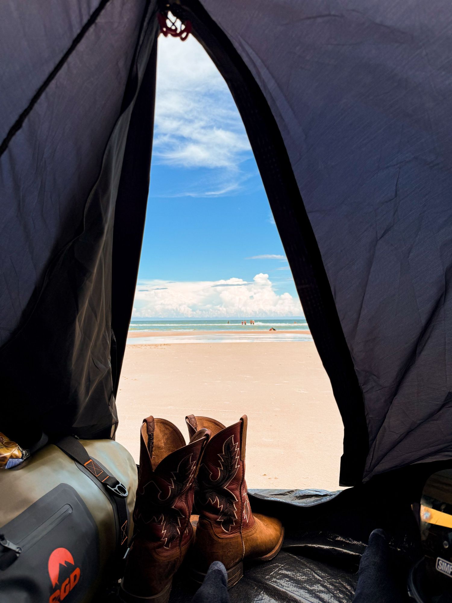 View from inside a tent of cowboy boots with a sunny beach ocean backdrop.