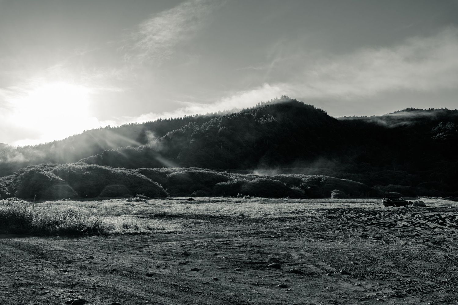 Misty black and white mountain landscape with sunlight breaking through clouds over a vast open valley floor.