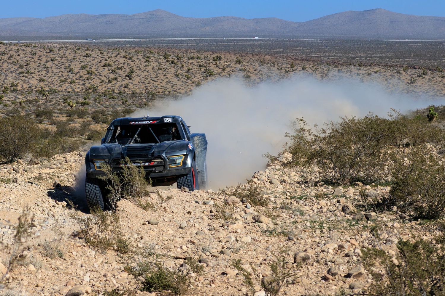 Race buggy navigating rocky desert landscape kicking up dust during off-road competition.