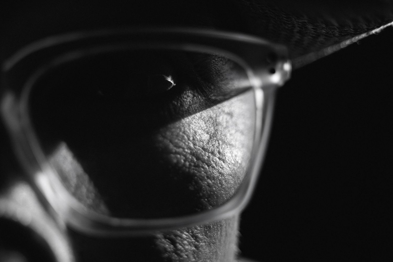 Extreme close-up black and white macro shot of glasses lens on a mans face under a hat.