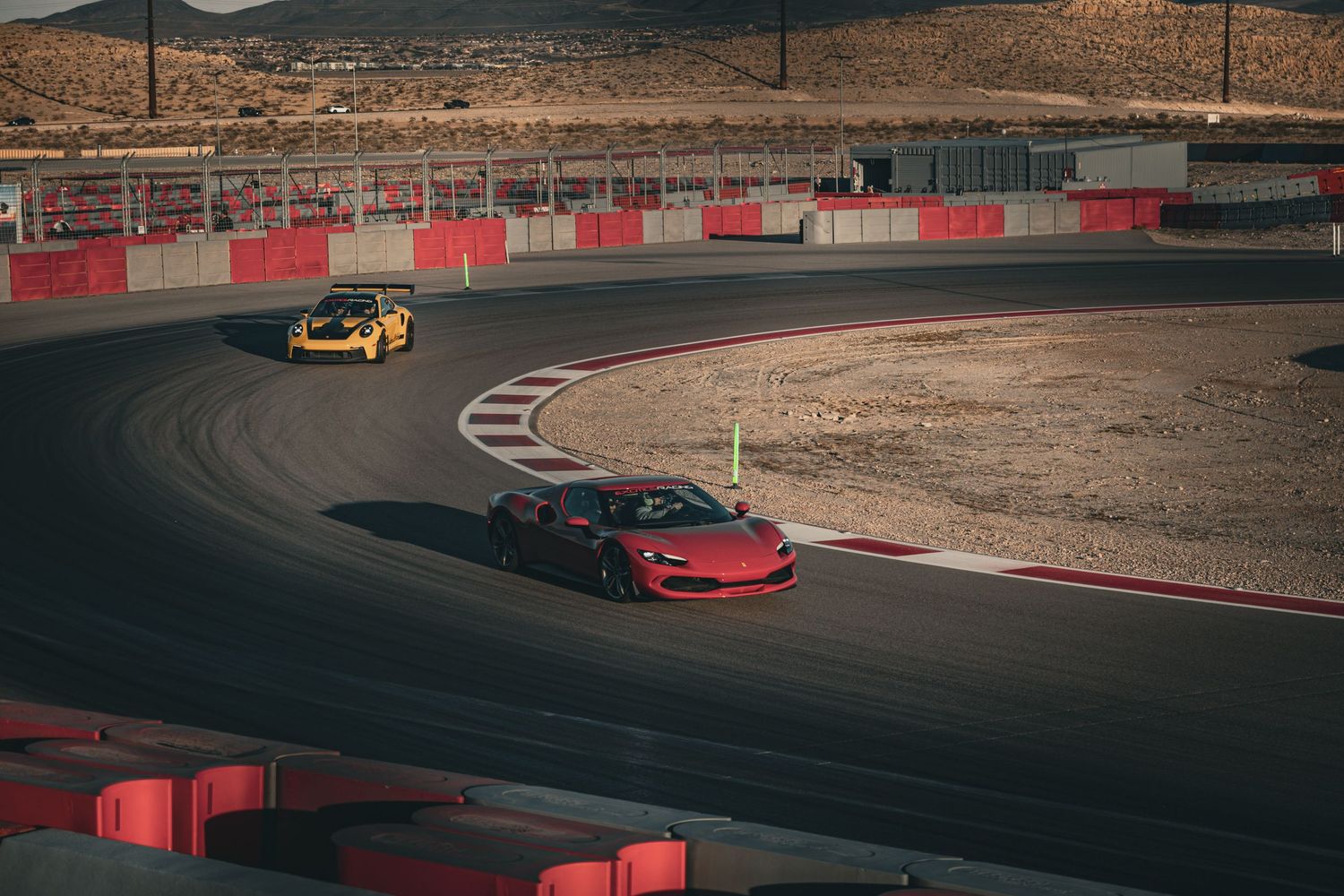 Red and yellow Ferrari supercars racing through a sweeping corner on a desert track circuit.