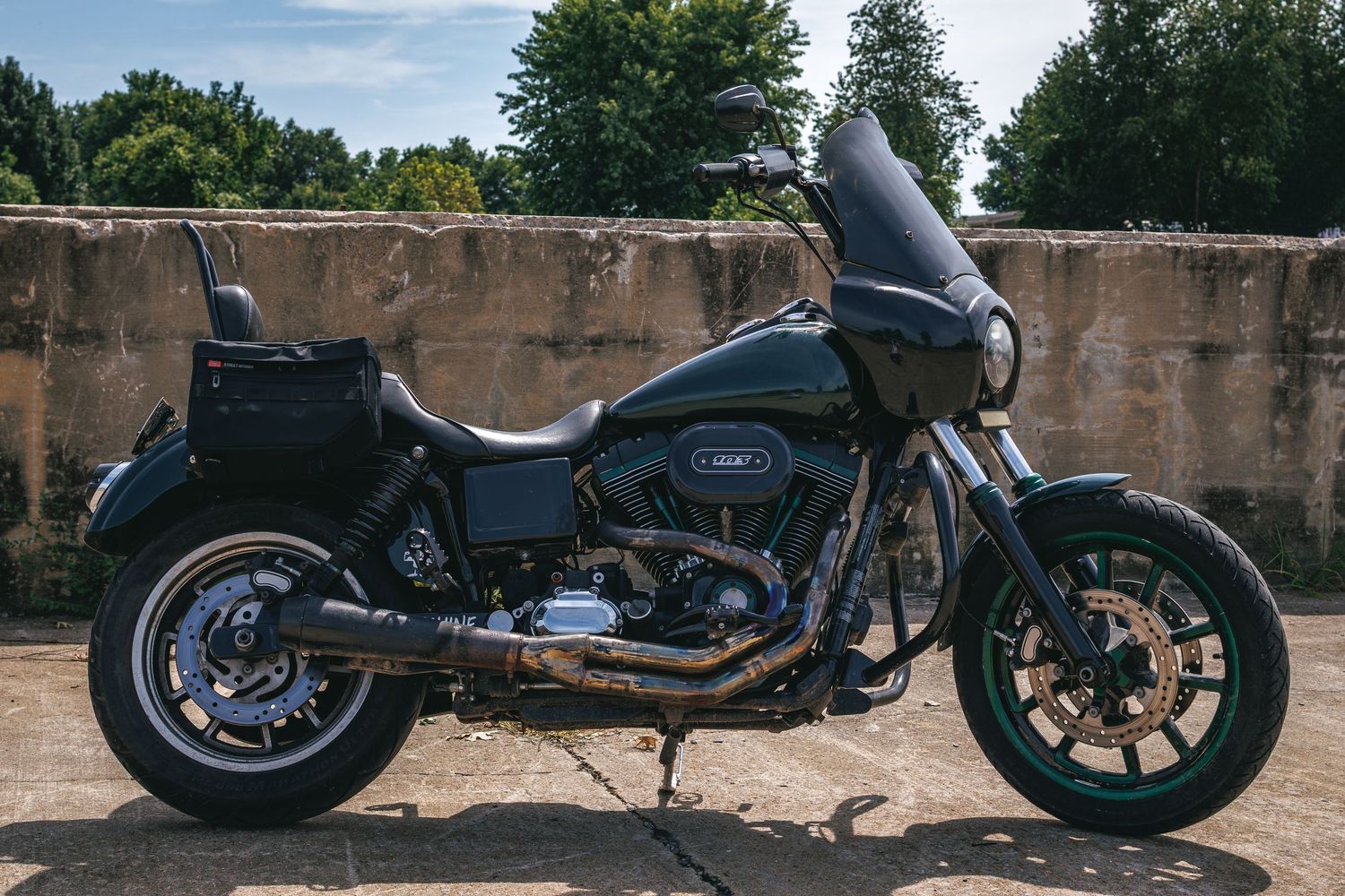 Custom matte black Harley-Davidson motorcycle with saddlebags parked outdoors against a weathered concrete wall.