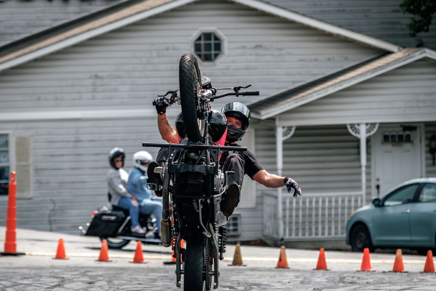 Motorcyclist performing a wheelie between traffic cones on a suburban street.