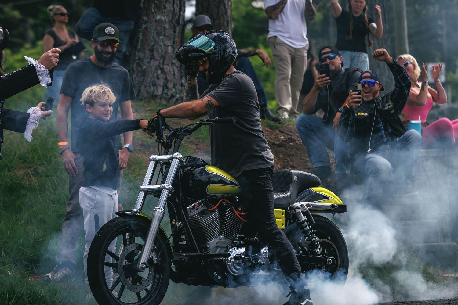 Harley-Davidson rider performing a smoky burnout for an outdoor crowd of spectators.