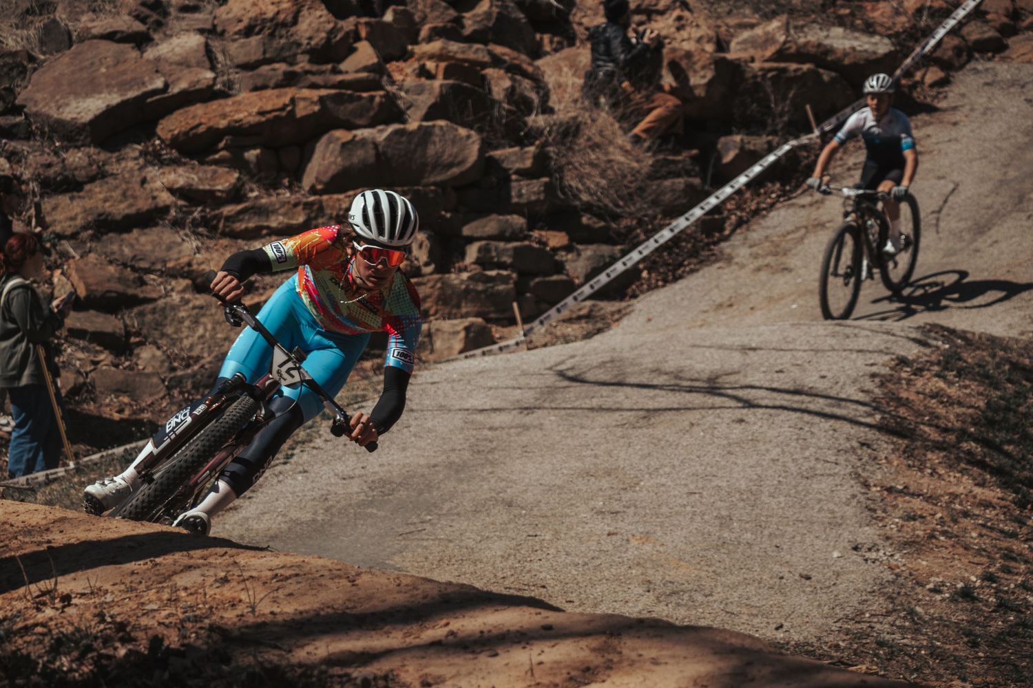 Mountain biker in colorful kit navigating a steep rocky descent during a competitive race.